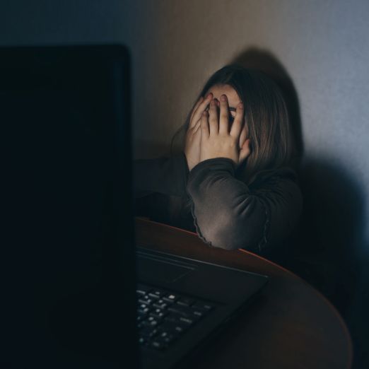 Bild: Ein Mädchen sitzt an einem Tisch vor einem Laptop und verbirgt ihr Gesicht in ihren Händen.