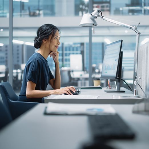 Eine Frau im Büro sitzend schaut auf ihrem Monitor
